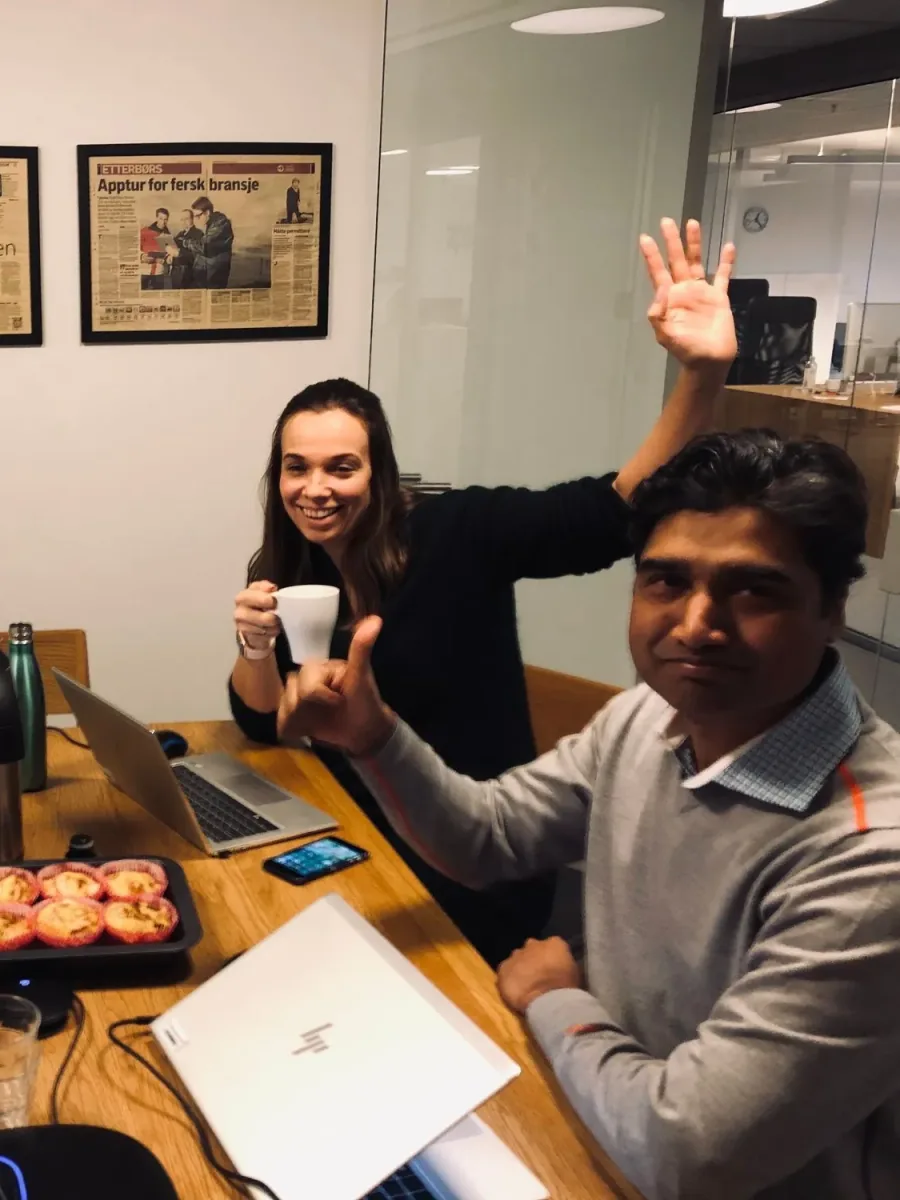 Two colleagues at a meeting table with laptops, coffee and muffins