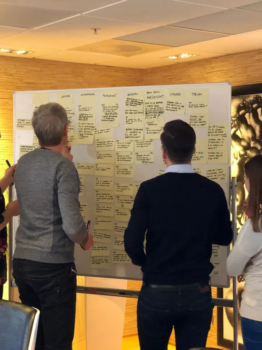 Three people standing at a whiteboard covered in handwritten sticky notes